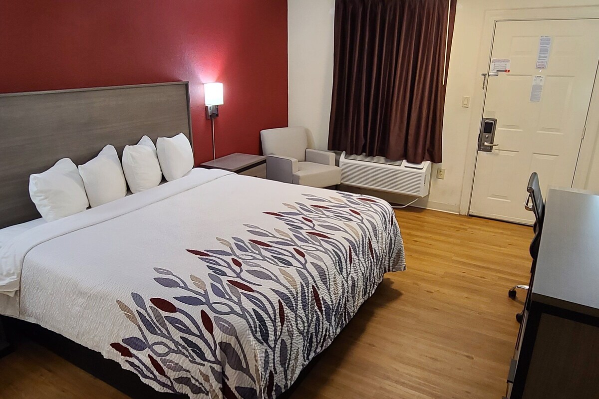 A hotel room with a large bed, a desk, a chair, a heater, and a door.