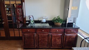 A kitchen with a wooden cabinet, a coffee machine, and a plant on the counter. - Red Roof Inn & Suites Cornelius – Lake Norman (Cornelius)