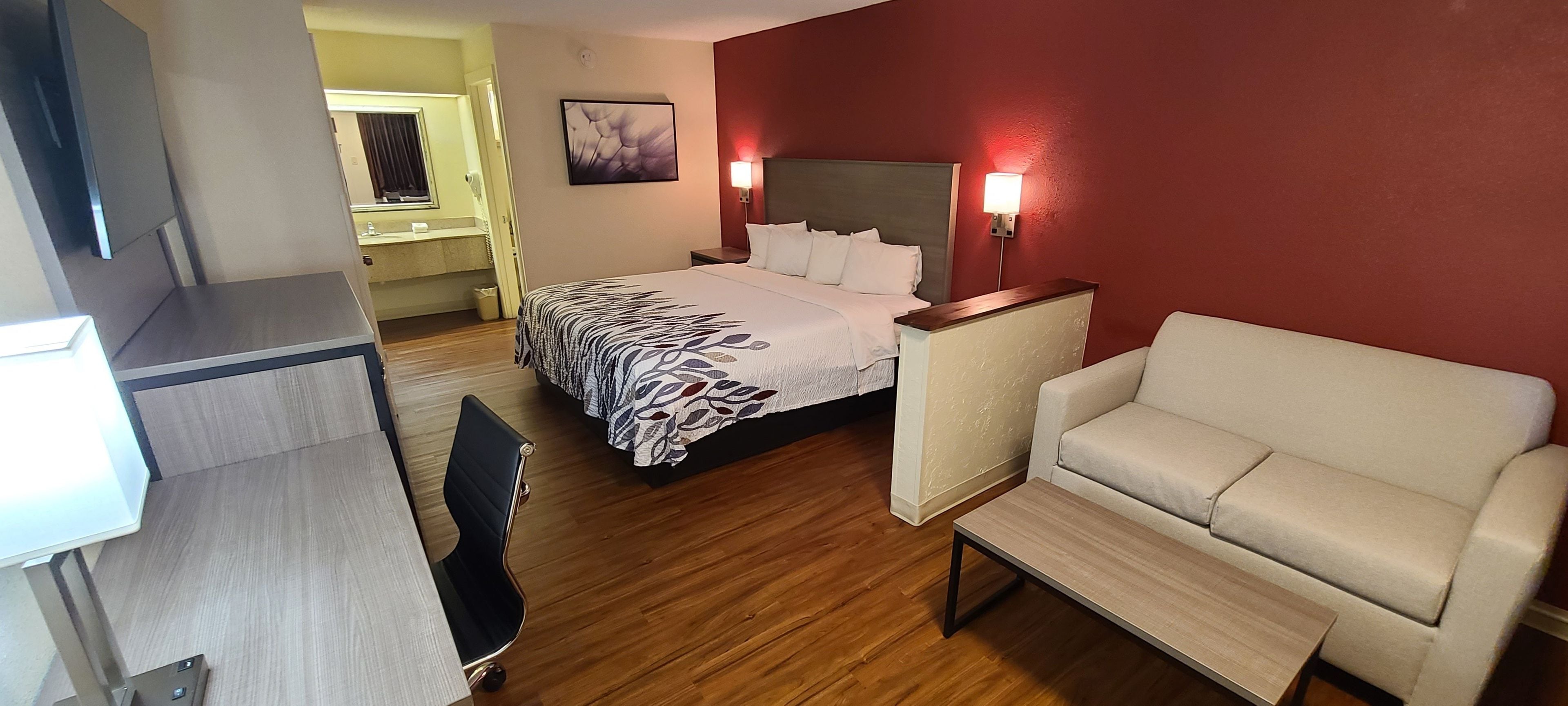 A hotel room with a bed, a chair, a desk, and a mirror.
