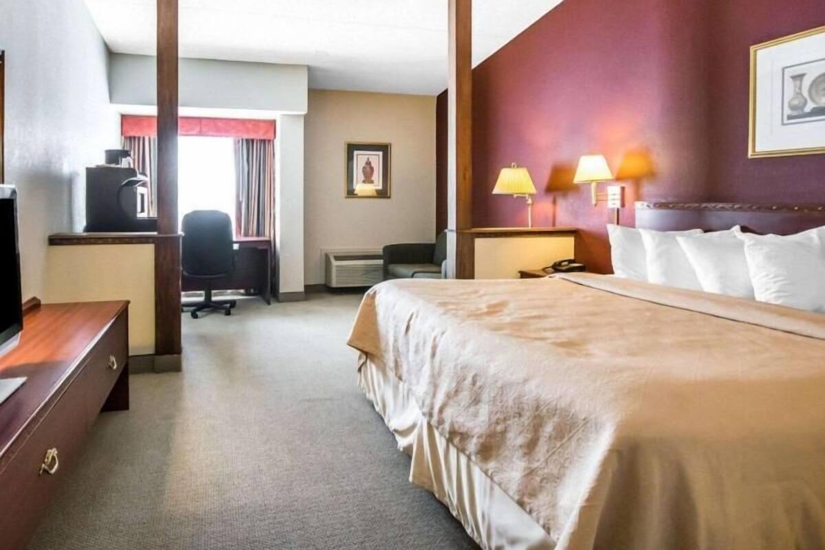 A hotel room with a bed, desk, chair, and a television.