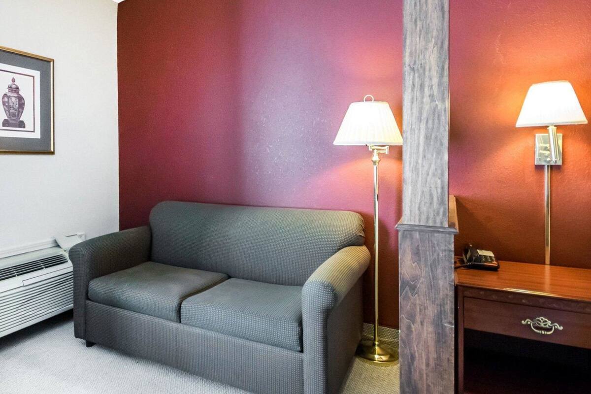 A room with a grey sofa, two floor lamps, a wooden nightstand, and a framed picture on the wall.
