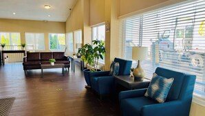 Amplia sala de estar con piso de madera oscura, un sofá de cuero marrón, un sillón azul y una mesita de centro. Hay plantas en macetas y una lámpara sobre una mesita auxiliar.