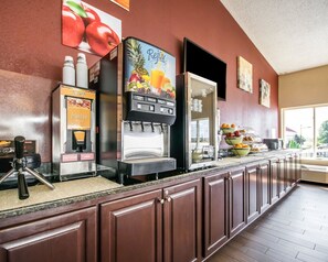 A breakfast bar with a waffle maker, a juice dispenser, and a fruit display.