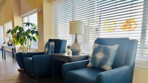 Un área de descanso moderna con sillones azules, una mesita con lámpara y plantas en macetas.