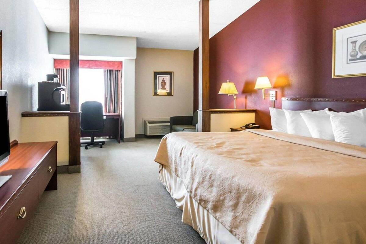 A hotel room with a bed, desk, chair, and a desk lamp.