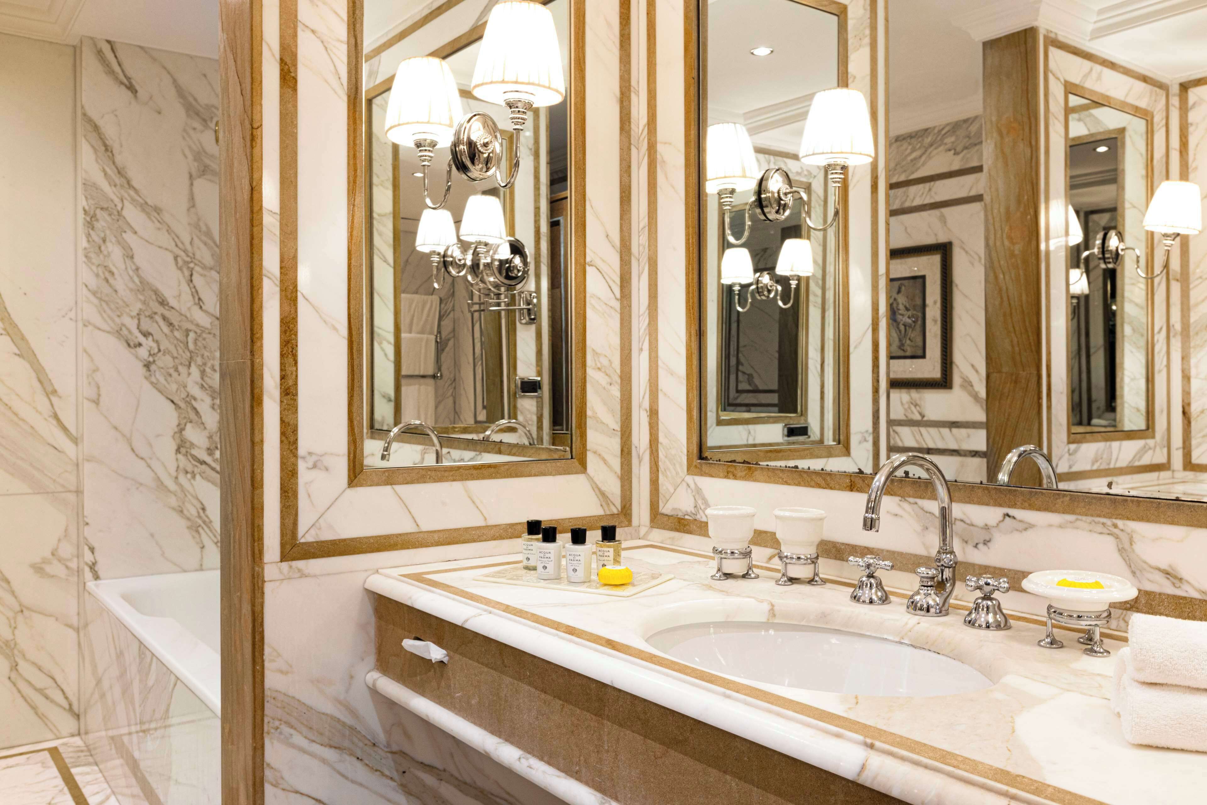 Ein luxuriöses Badezimmer mit einem großen Marmorwaschbecken, mehreren Spiegeln und stilvollen Leuchten.