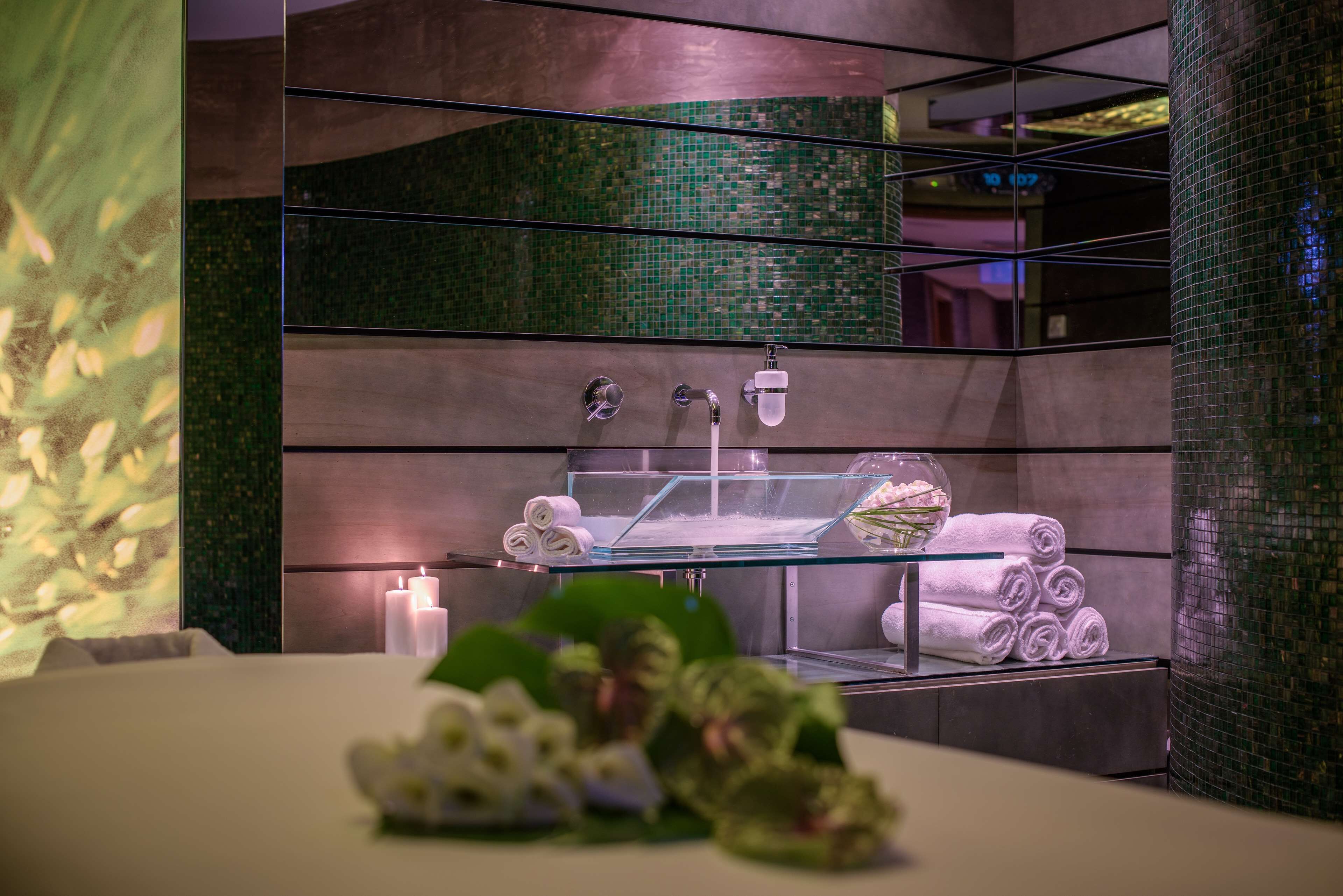 Un bagno moderno con un lavandino in vetro, diversi asciugamani e un vaso decorativo.