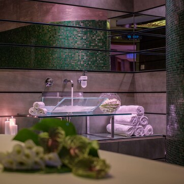 A modern bathroom with a glass sink, multiple towels, and a decorative vase.