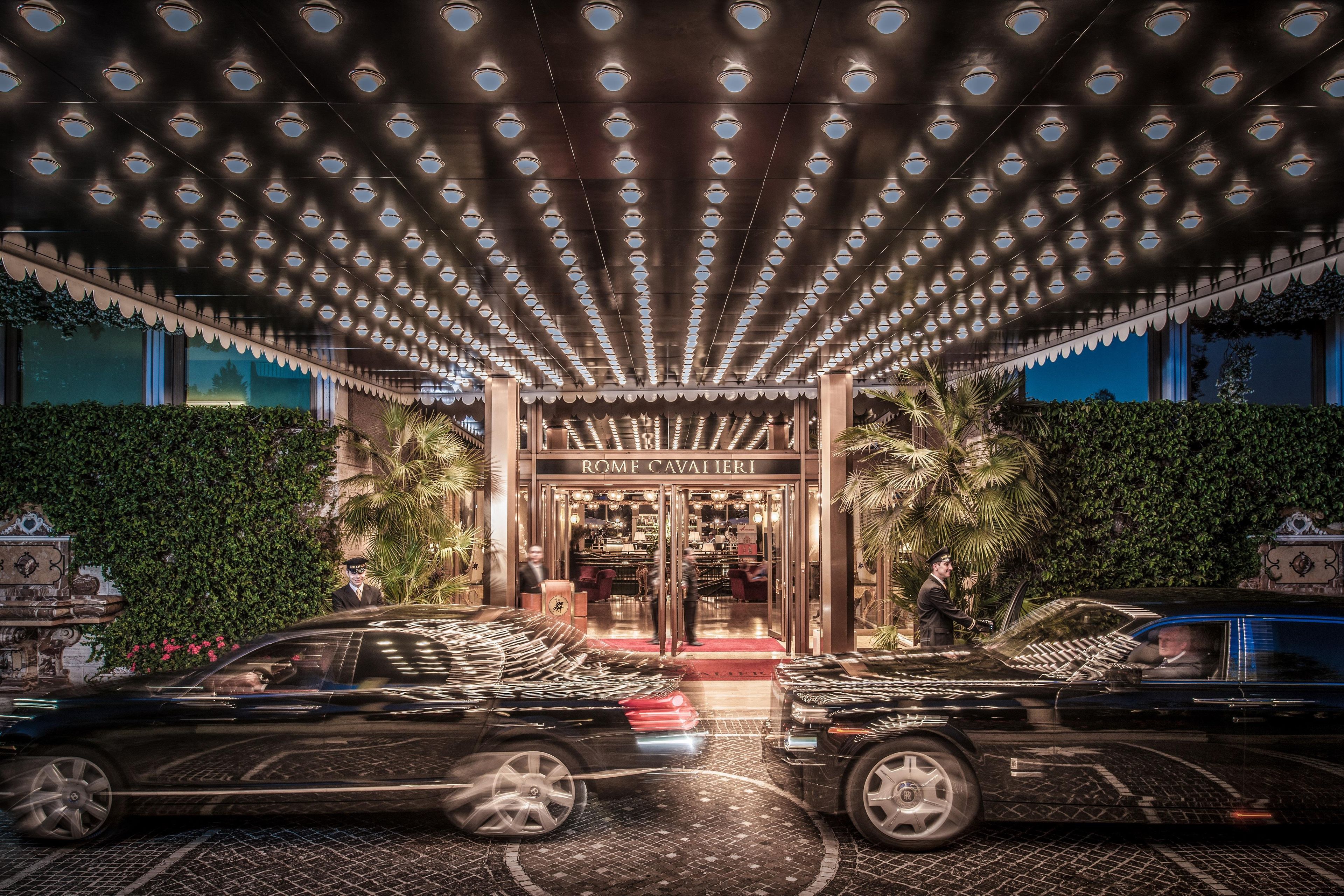 A grand entrance with a canopy of lights, a red carpet, and two luxury cars parked at the entrance.