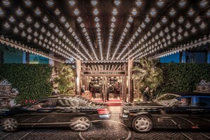 A grand entrance with a canopy of lights, a red carpet, and two luxury cars parked at the entrance.