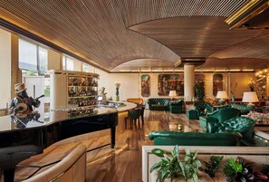 A spacious lobby with a piano, green sofas, a bar area, and a large mirror.