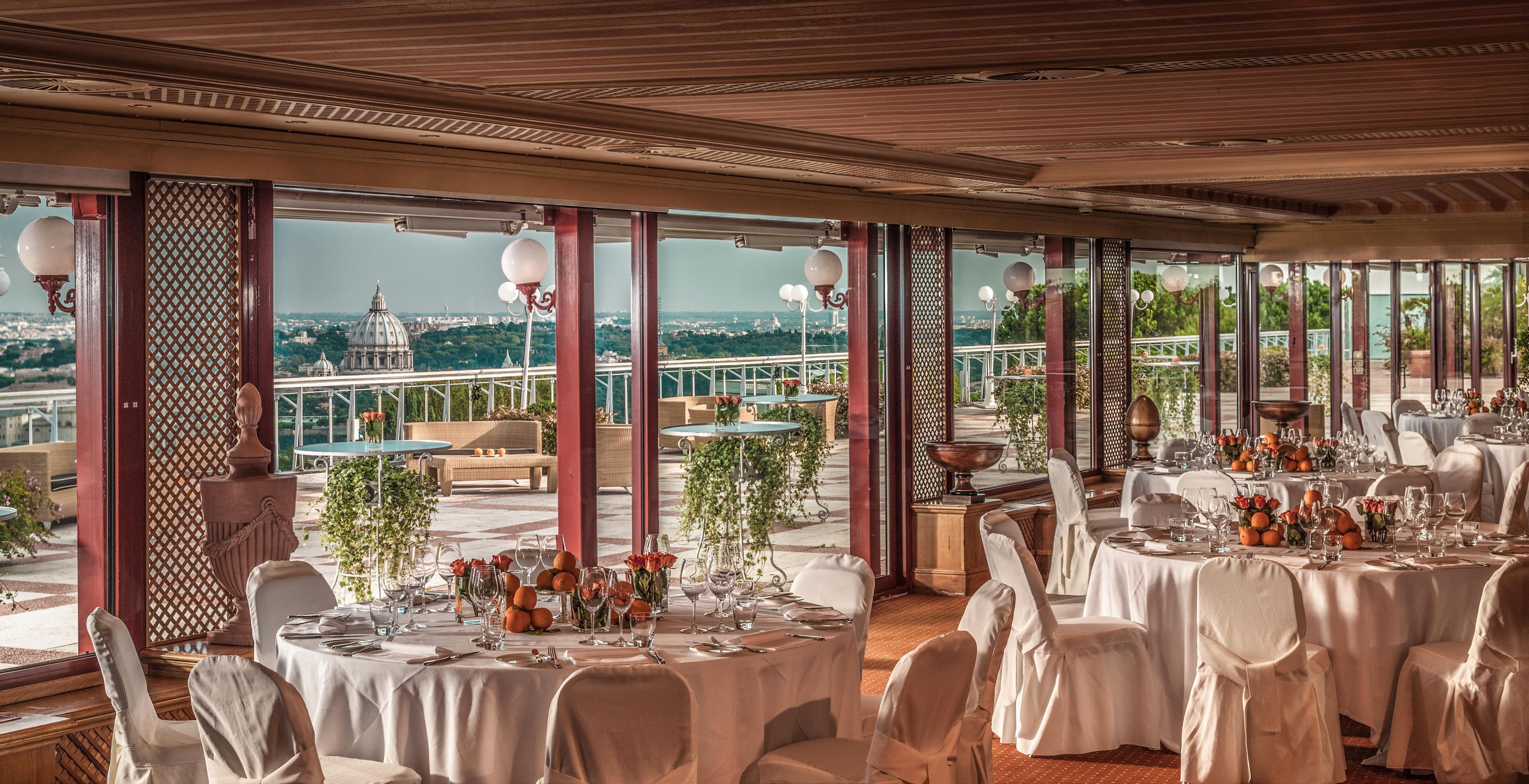 A restaurant with round tables set for dining, large windows offering a city view, and a balcony with outdoor seating.