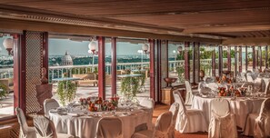 A restaurant with round tables set for dining, large windows offering a city view, and a balcony with outdoor seating.
