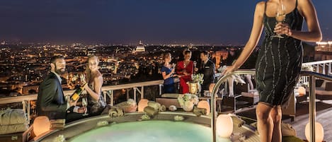 A rooftop terrace with a hot tub, seating area, and a city view.