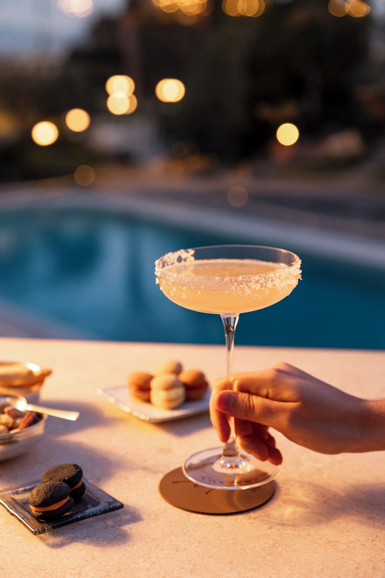 Et cocktailglas med saltet kant på et bord nær en pool.