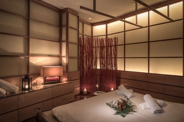 Habitación de hotel moderna con cabecera de madera, una mesita de noche con lámpara y una cama con toallas ordenadas.