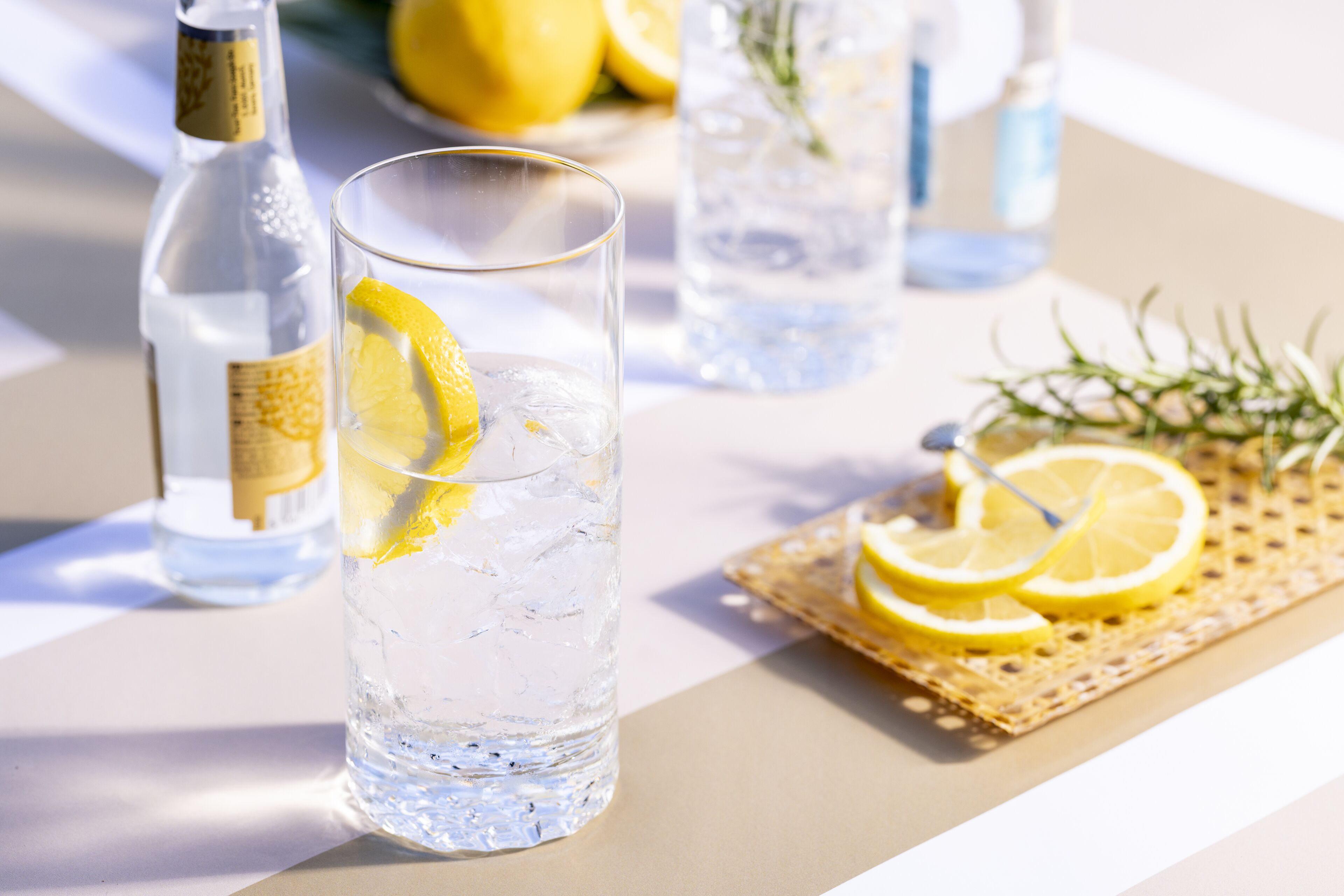 Un verre d’eau avec une tranche de citron, une bouteille d’eau et un autre verre d’eau avec une tranche de citron, le tout posé sur une table.
