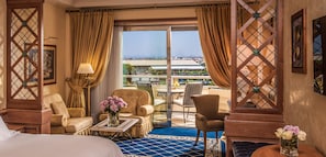 A hotel room with a bed, two armchairs, a coffee table, a vase of flowers, and a view of the city through large windows.