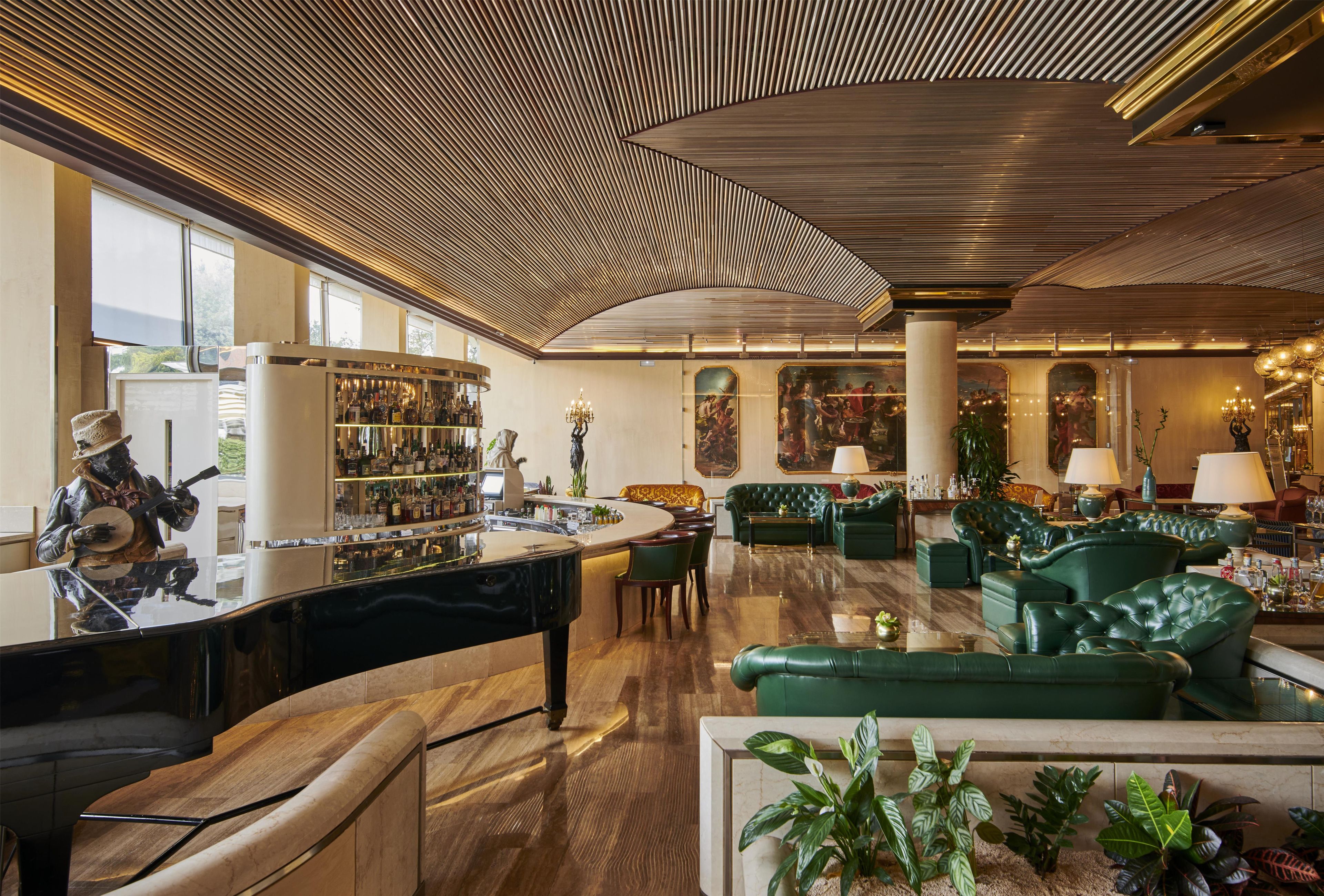 Eine Bar mit Klavier, grünen Sofas und einer Bar, an der Flaschen stehen.