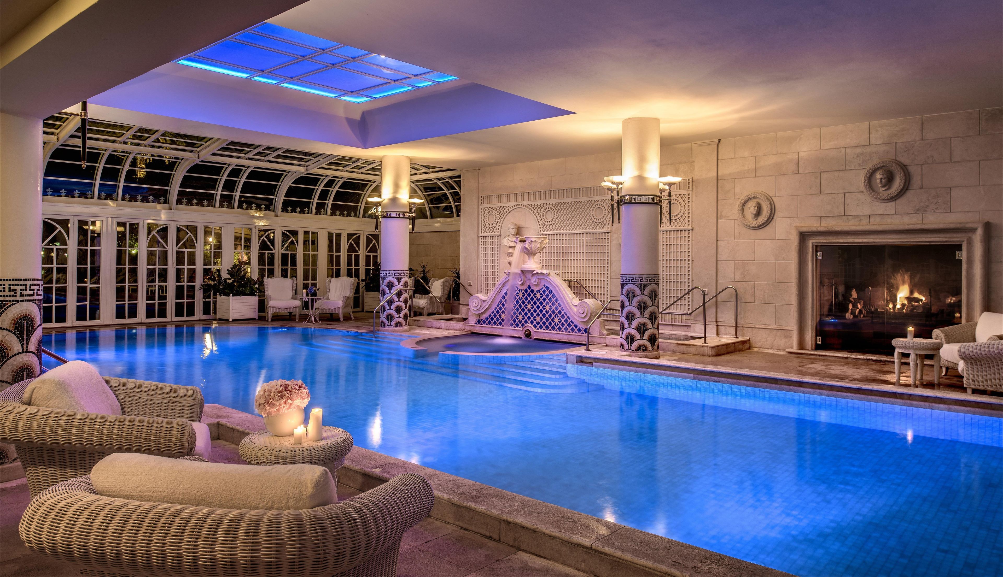 Une piscine intérieure dotée de chaises longues, d’une fontaine décorative et d’une cheminée.
