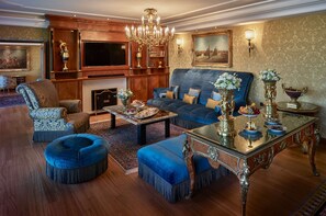 A luxurious living room with a blue sofa, matching ottomans, a wooden coffee table, and a chandelier.