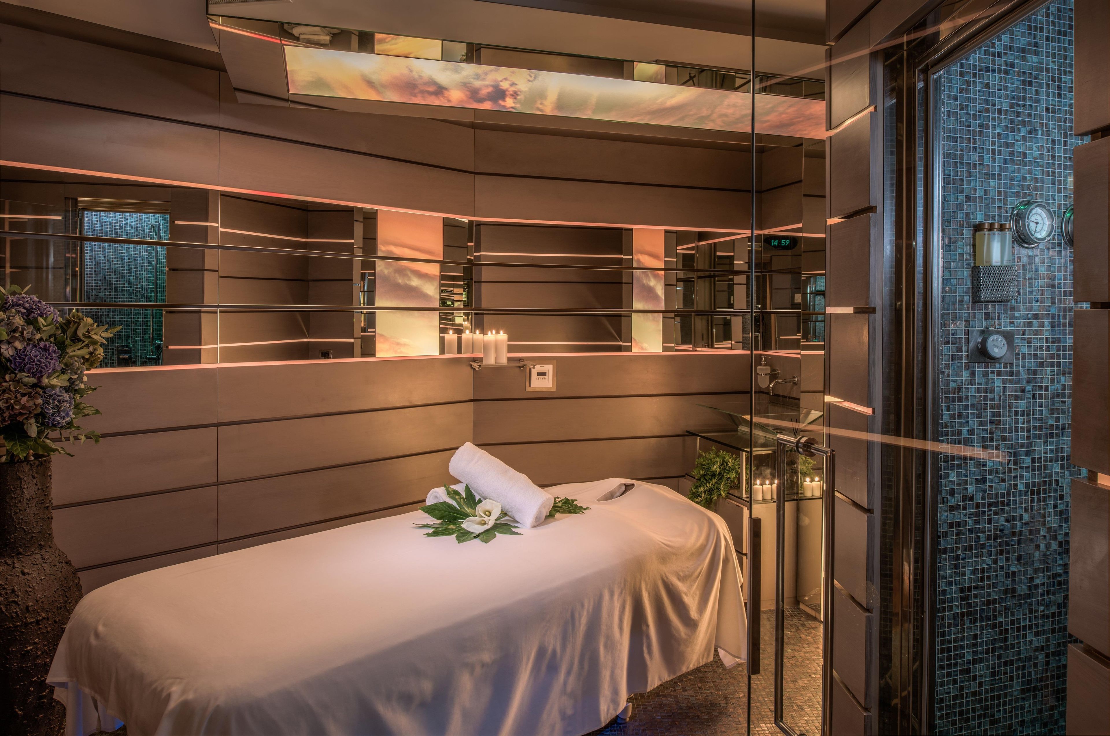 A modern spa room with a massage table, a large mirror, and a glass partition.