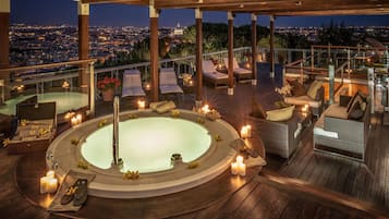 A rooftop terrace with a hot tub, lounge chairs, and candles.