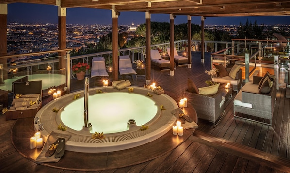 A rooftop terrace with a hot tub, lounge chairs, and candles.