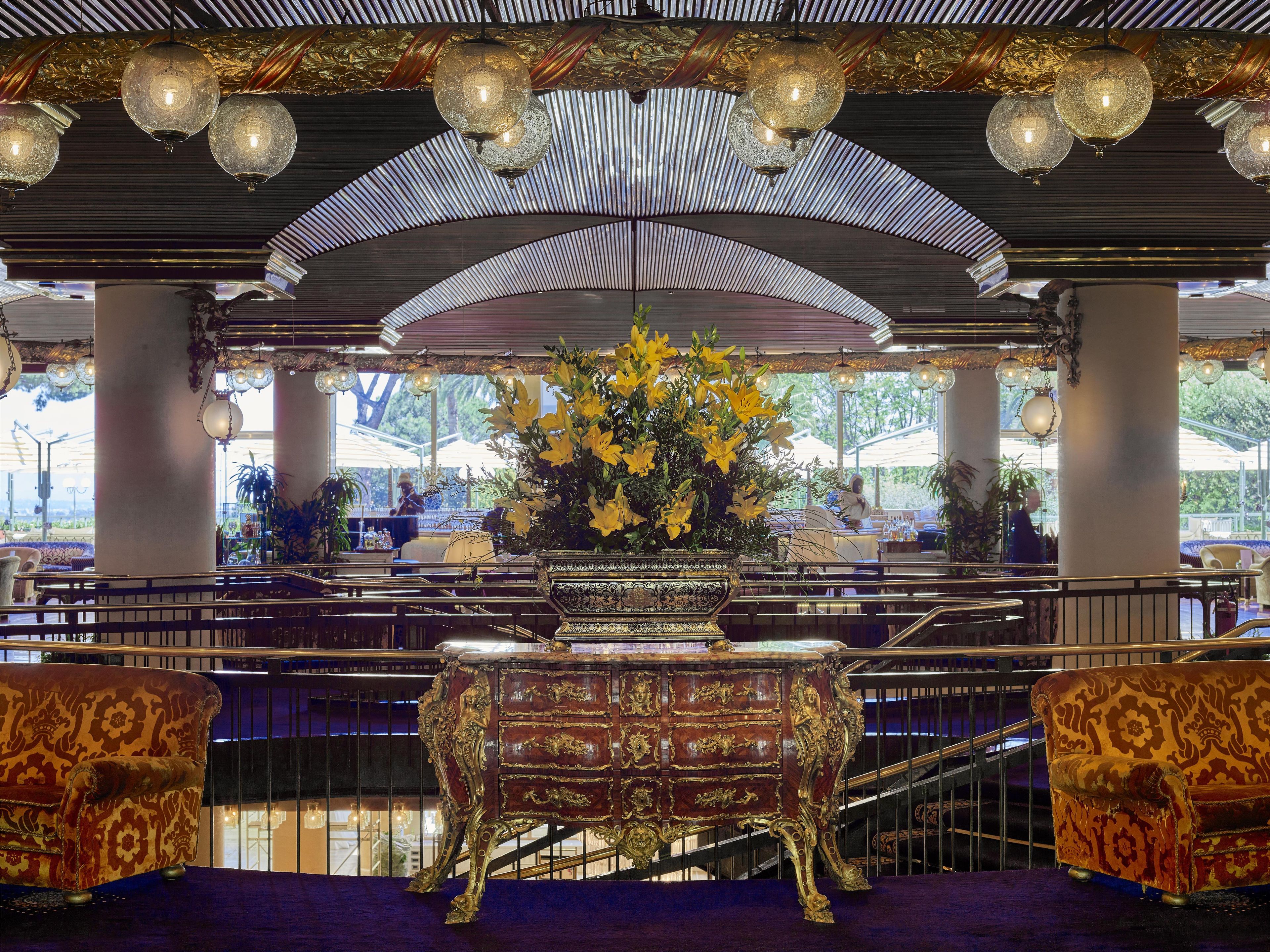 Interior ornamentado com uma escadaria imponente, um arranjo floral grande e móveis clássicos.