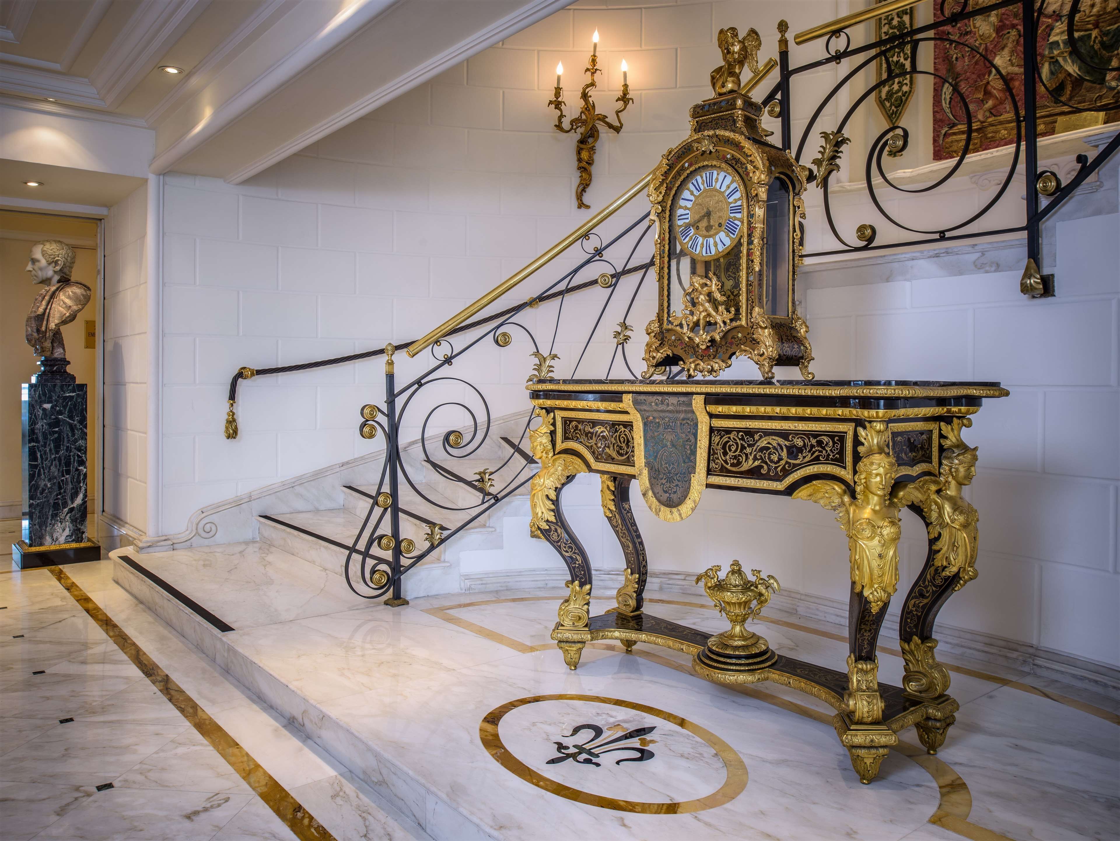 A grand staircase with ornate gold railings and a large, gilded clock.
