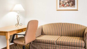 Een kamer met een houten bureau, een fauteuil, een gestreepte bank, een kamerbreed tapijt en een schilderij in een lijst aan de muur.