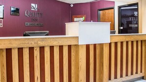 Een receptiebalie met een houten paneelontwerp, een paarse muur met het bord 'Quality Inn' en een receptiecounter.