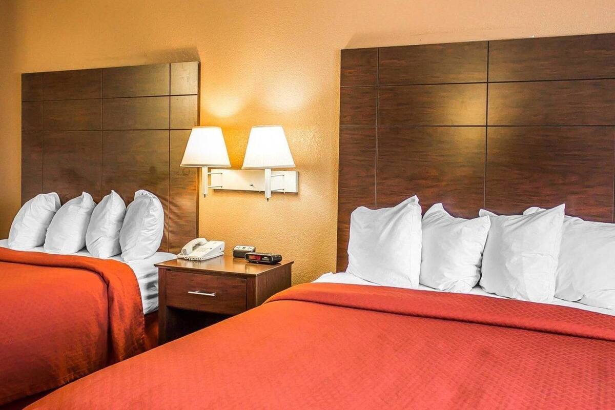 Quarto de hotel com duas camas, uma mesinha de cabeceira, um telefone e luminárias fixadas na parede.
