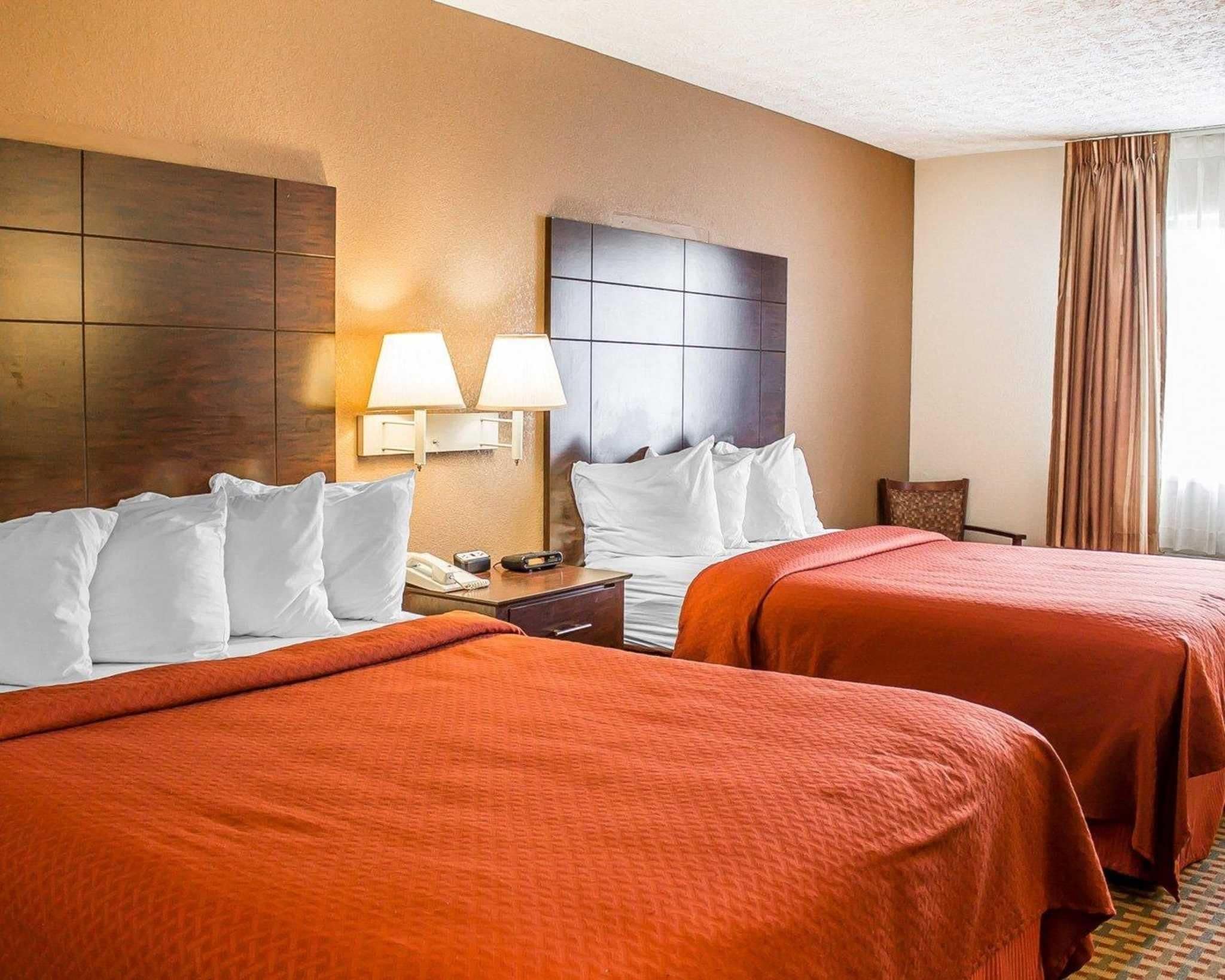 A hotel room with two beds, a nightstand, a lamp, and a chair.