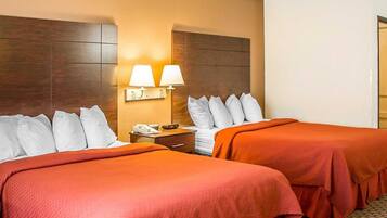 A hotel room with two beds, a nightstand with a phone and lamp, and a wall-mounted light fixture.