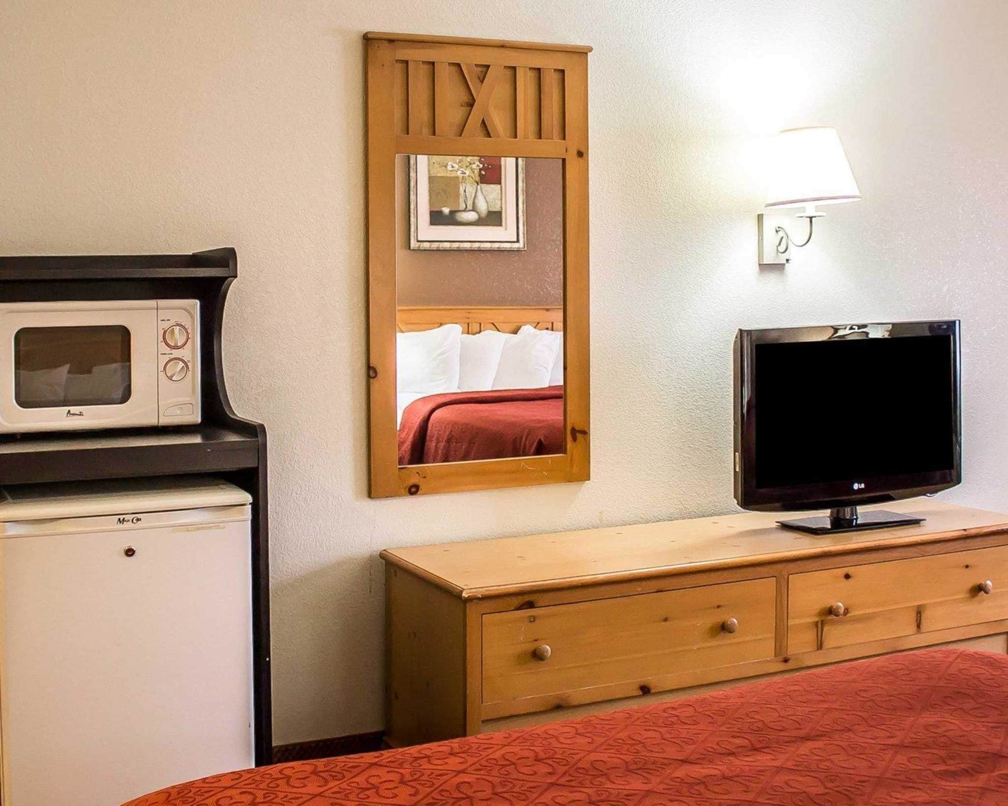 A hotel room with a bed, a wooden dresser, a television, a microwave, and a mirror.