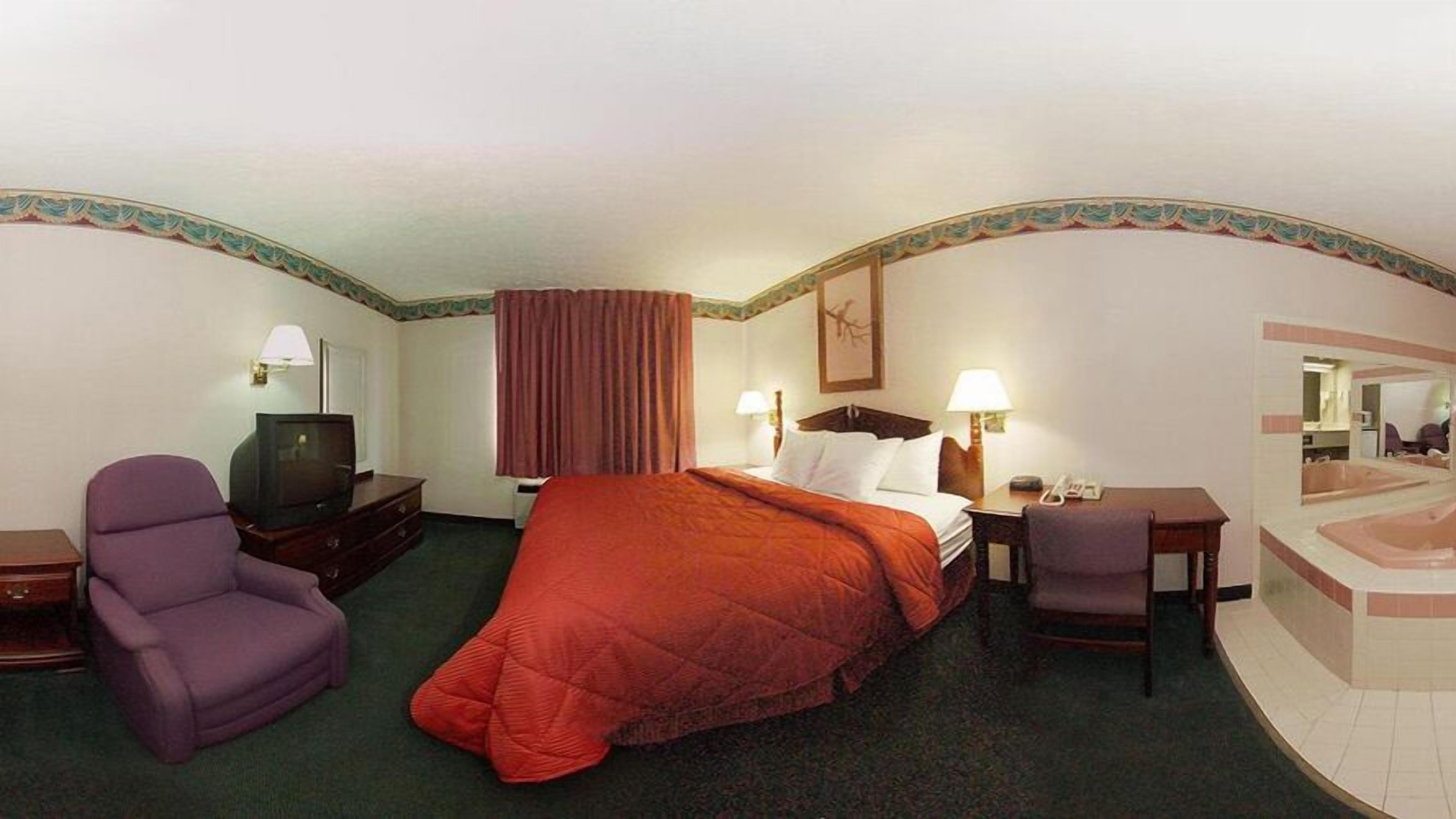 Una habitación de hotel con cama, televisión, escritorio, silla y baño con bañera.