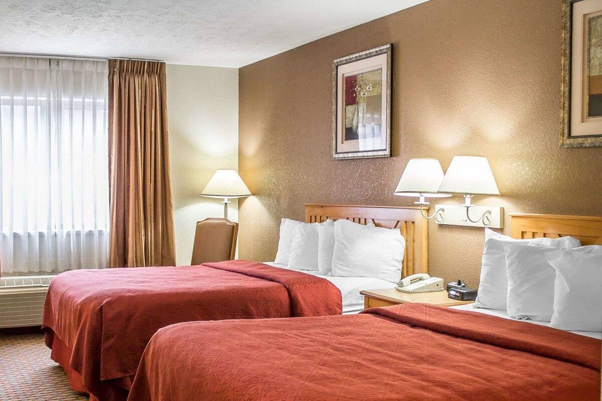 Quarto de hotel com duas camas, cabeceira, luminárias de cabeceira, telefone e um quadro na parede.