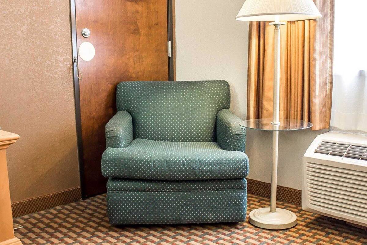 Um quarto com uma poltrona verde, um abajur de chão e um aparelho de ar condicionado branco.