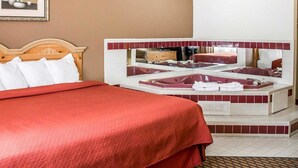 Een hotelkamer met een groot bed, een zithoek met een rode bank, een badkuip en een spiegel die de kamer reflecteert.