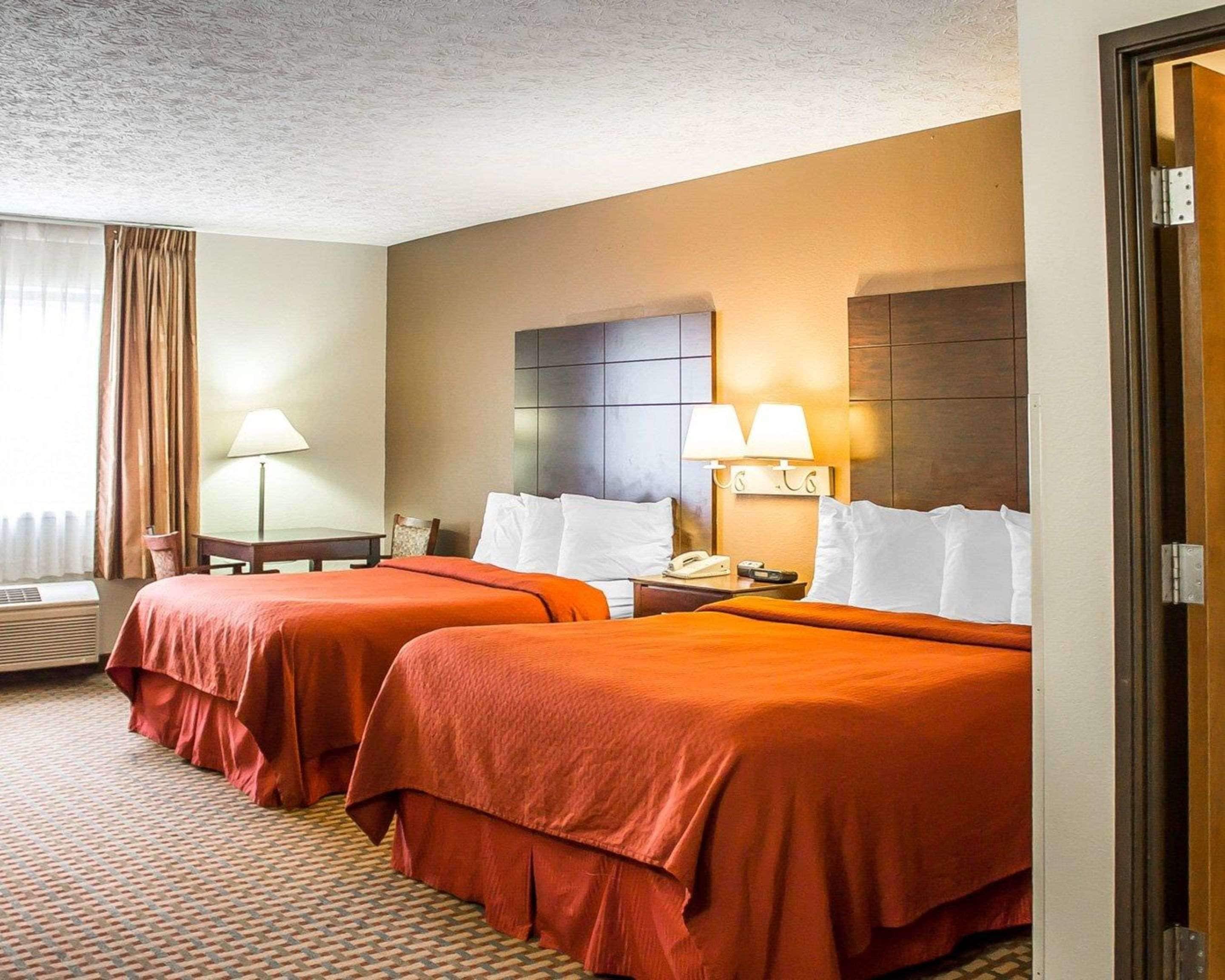 A hotel room with two beds, a desk, a lamp, and a phone on the nightstand.