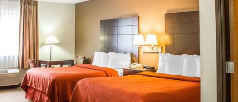 A hotel room with two beds, a desk, a lamp, and a phone on the nightstand.