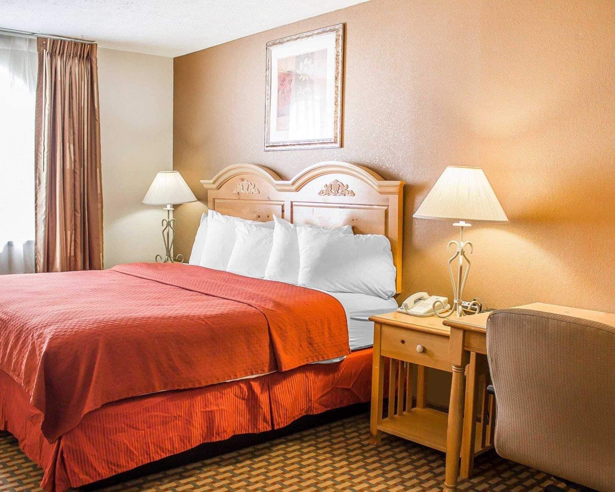 A hotel room with a large bed, two bedside tables with lamps, a chair, and a framed picture on the wall.