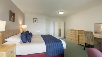 Una habitación de hotel con una cama, mesitas de noche, un aparador, una silla, un escritorio y un espejo.