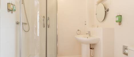 Un baño con cabina de ducha de vidrio, un lavamanos blanco y un inodoro.