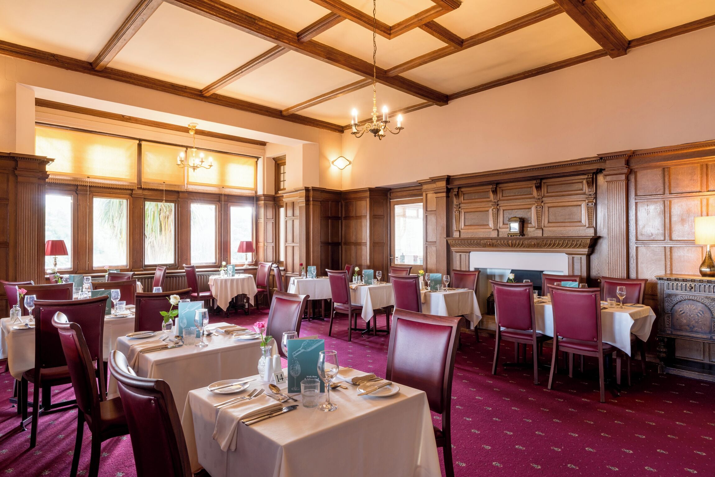 A dining area with tables set for service, wooden paneling, and a chandelier.