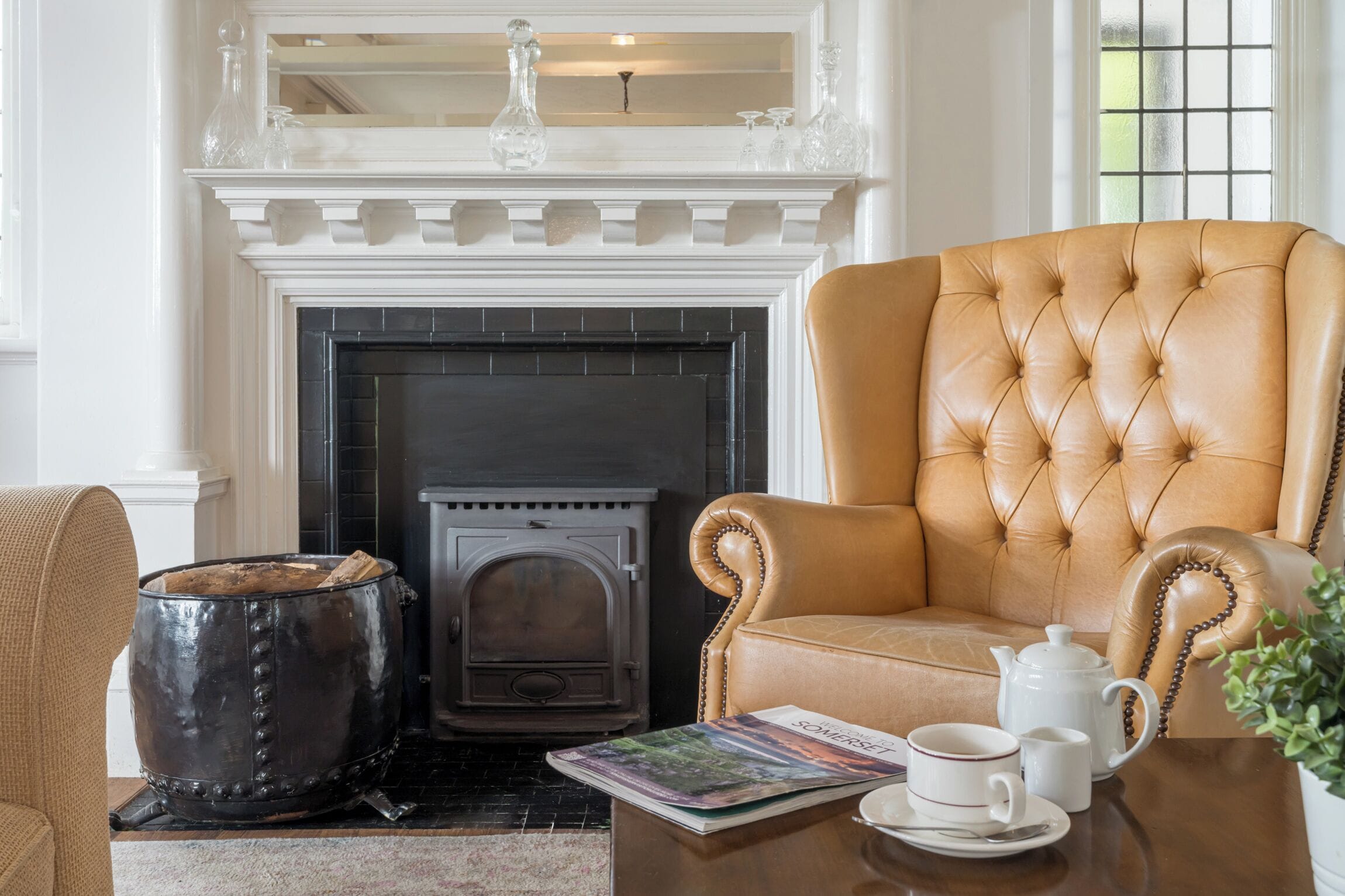 A room with a fireplace, a leather armchair, a table with a teapot, cups, and a magazine.