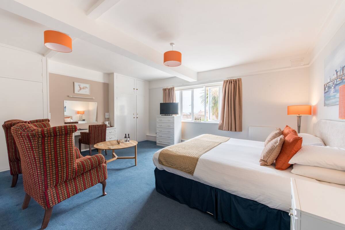 A hotel room with a bed, two chairs, a desk, a TV, and a window with curtains.
