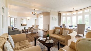A spacious living room with a fireplace, comfortable seating, and large windows. - Northfield Hotel (Minehead)