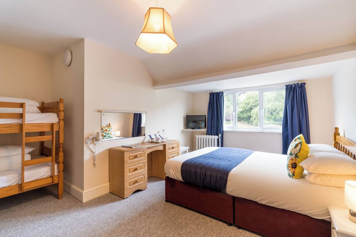 A bedroom with a bunk bed, a desk, a dresser, a TV, and a window with curtains.